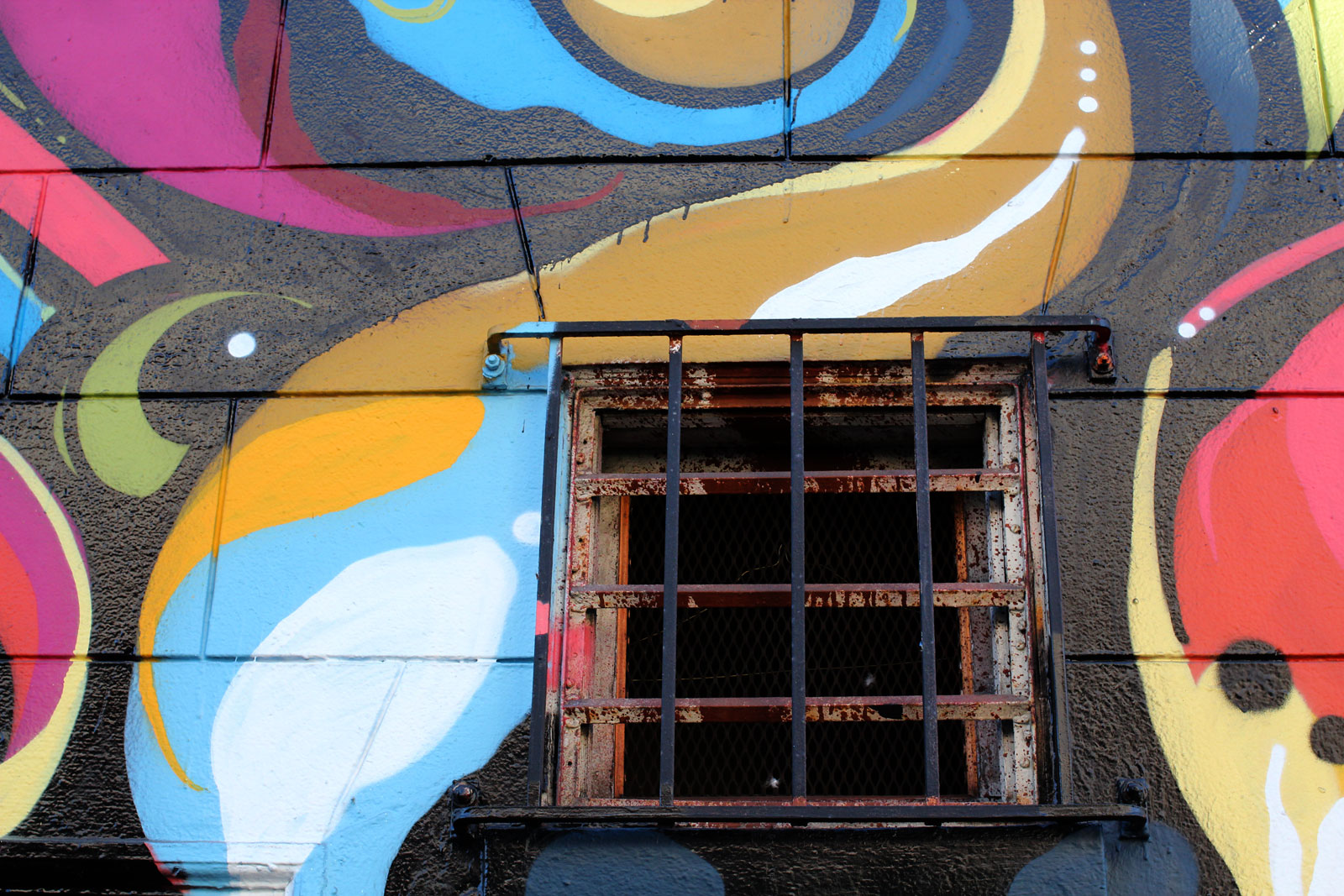 A barred window in a colorfully muraled brick wall