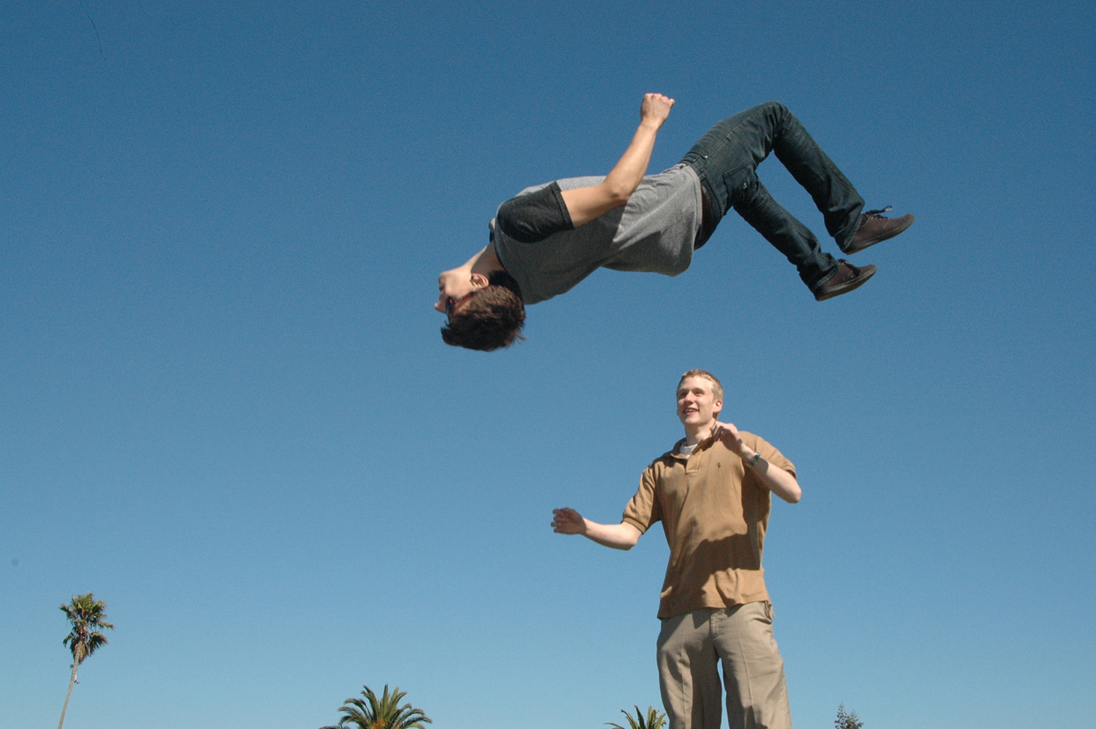 Image shows a man doing a back flip on a trampoline