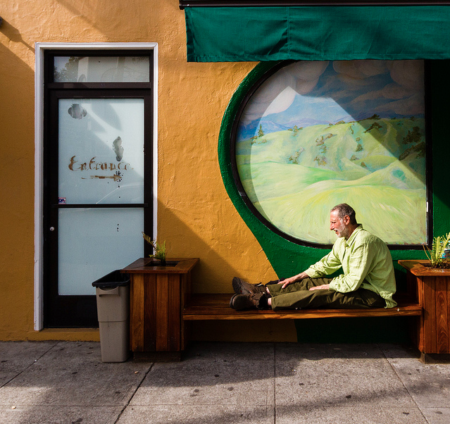 A man sits on a bench in front of a mural.