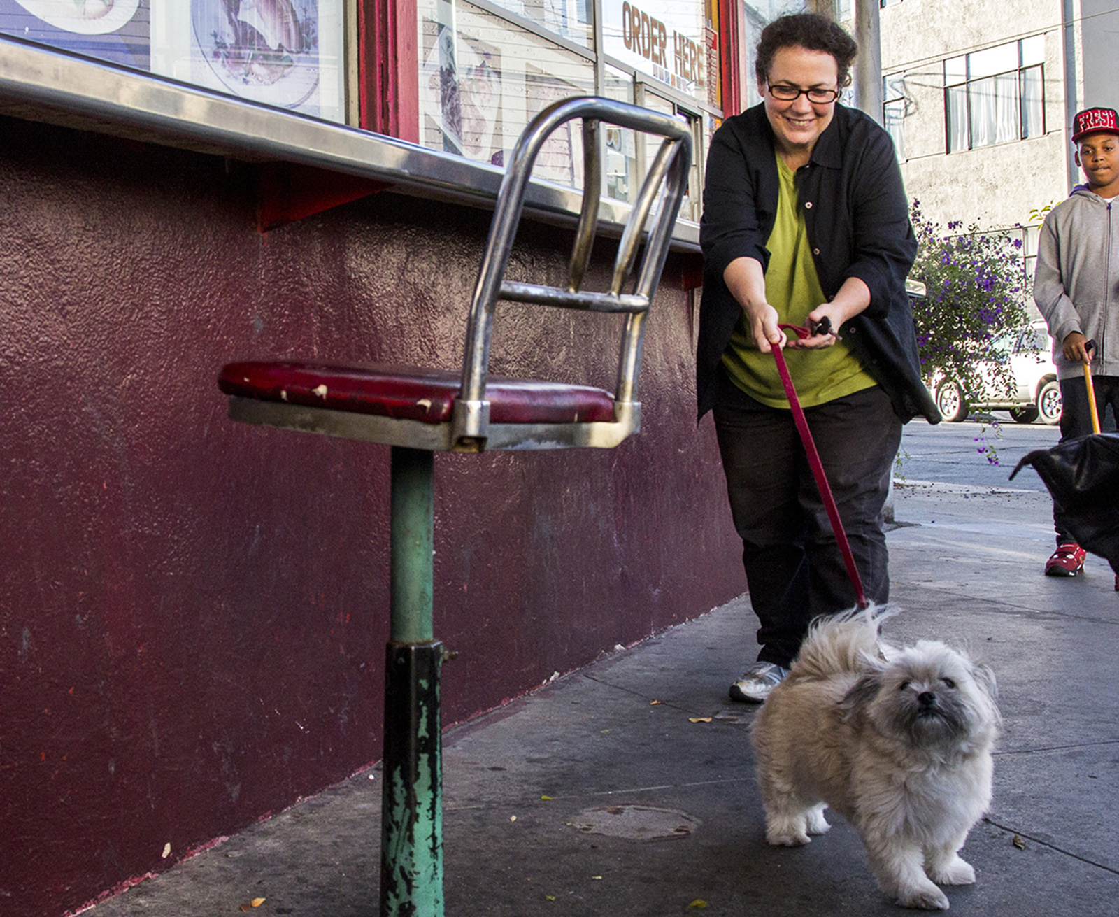 A lady tries to restrain her very happy puppy dog on a red leash.