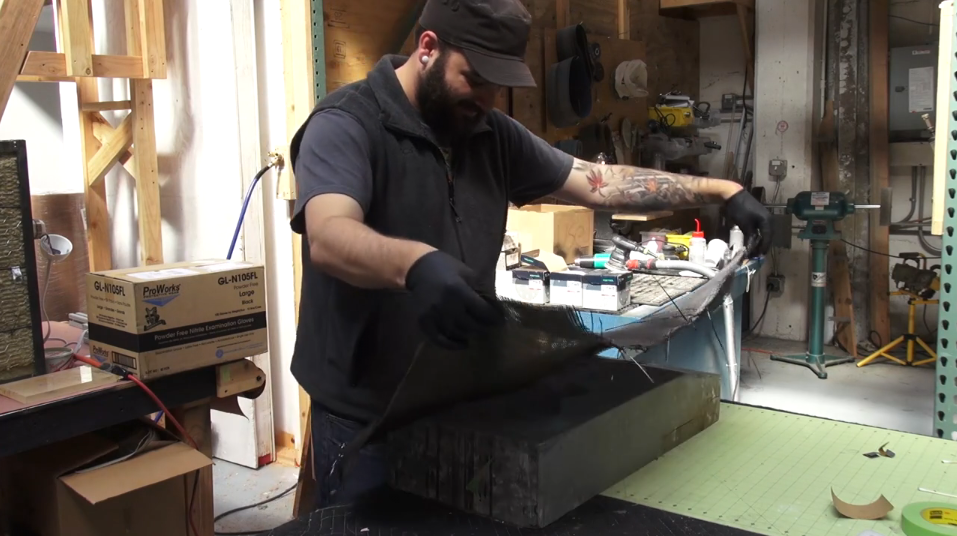 Image shows a man putting carbon fiber into a guitar mold.