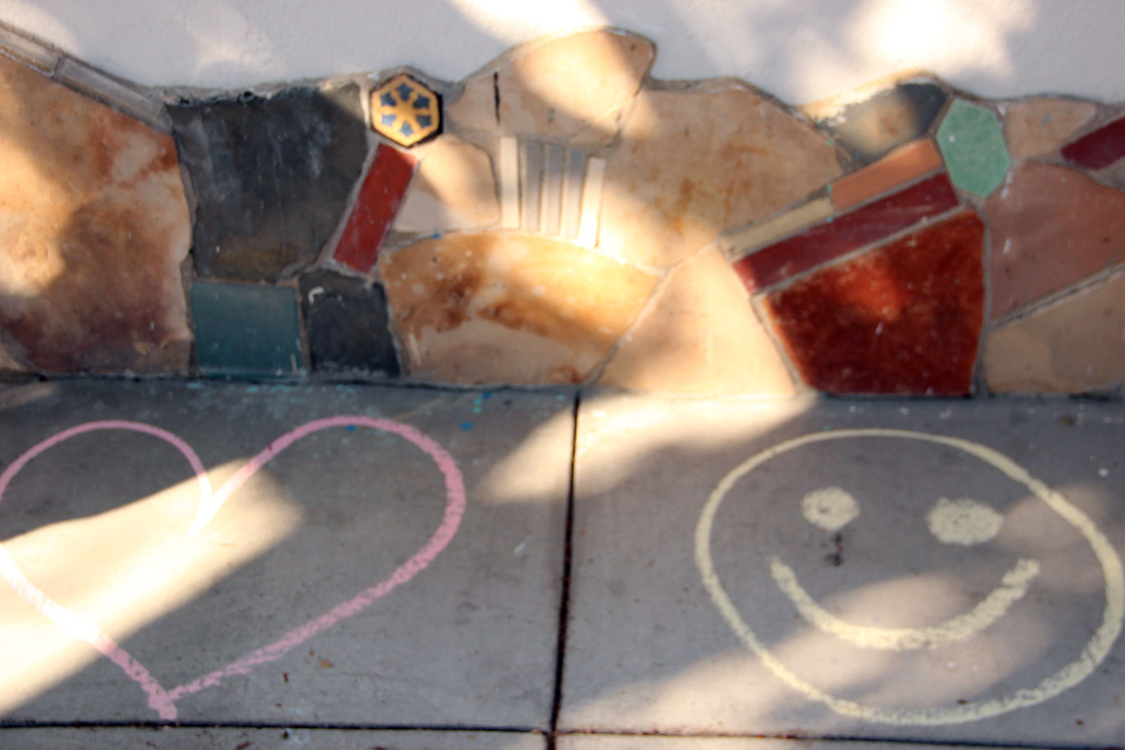 Chalk drawing os a red heart and a yellow smiley face on the sidewalk.