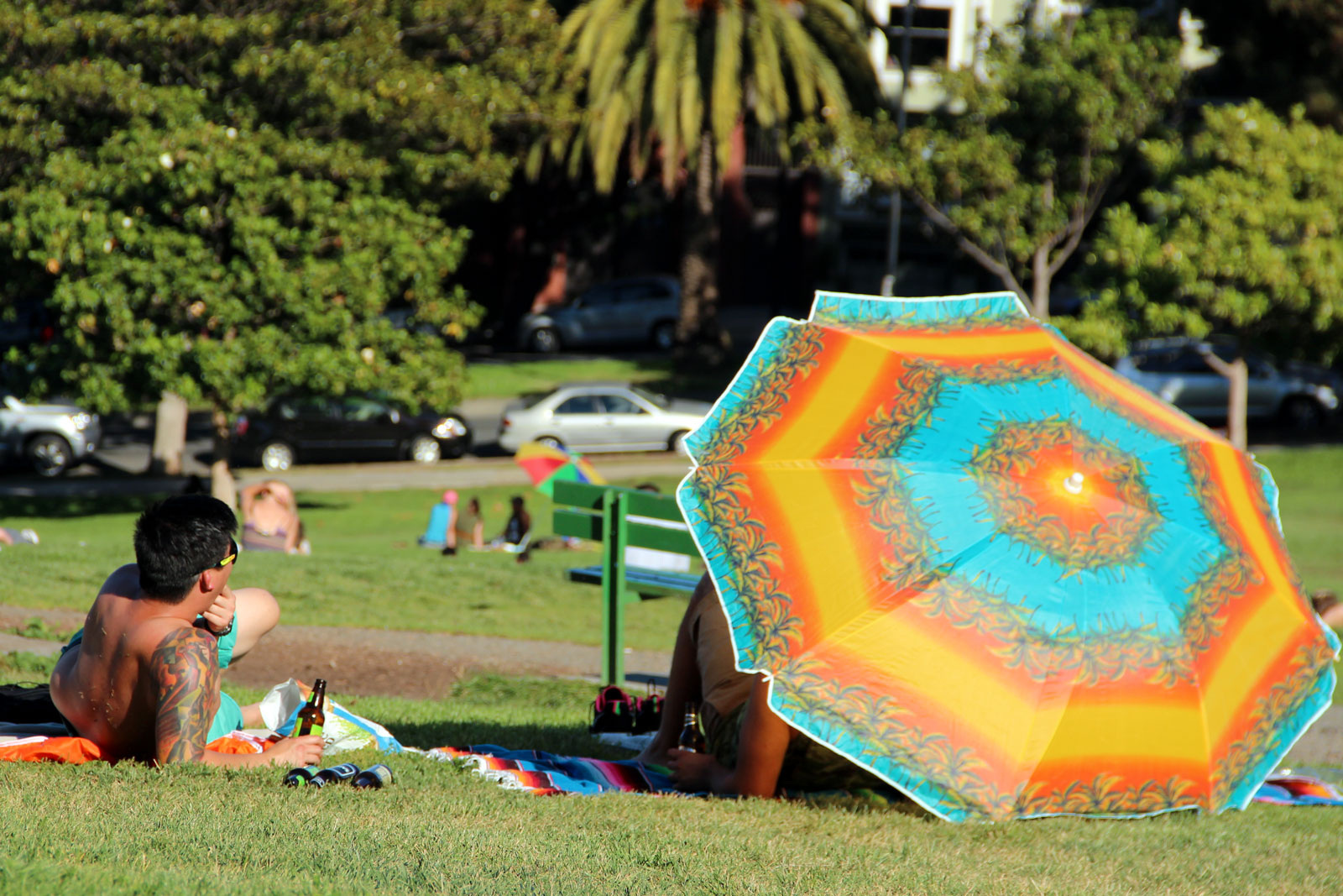 A man sits next to a bright beach umbrella.