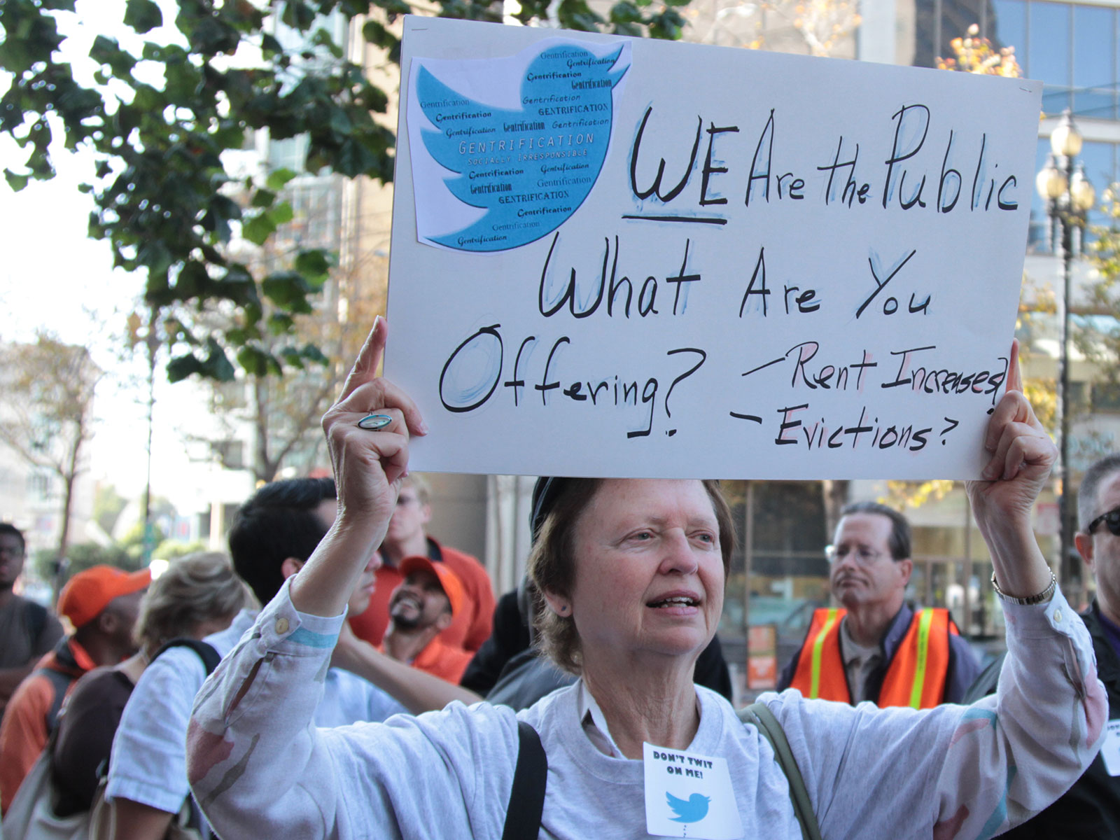 Woman holding sign that reads "we are the public, what are you offering?"