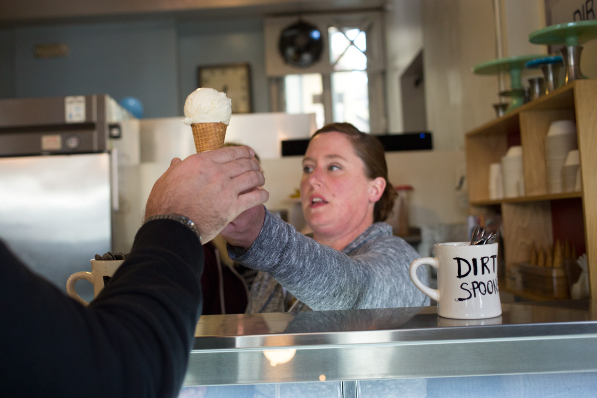 A woman hands an ice cream cone to a customer over a counter inside a shop.
