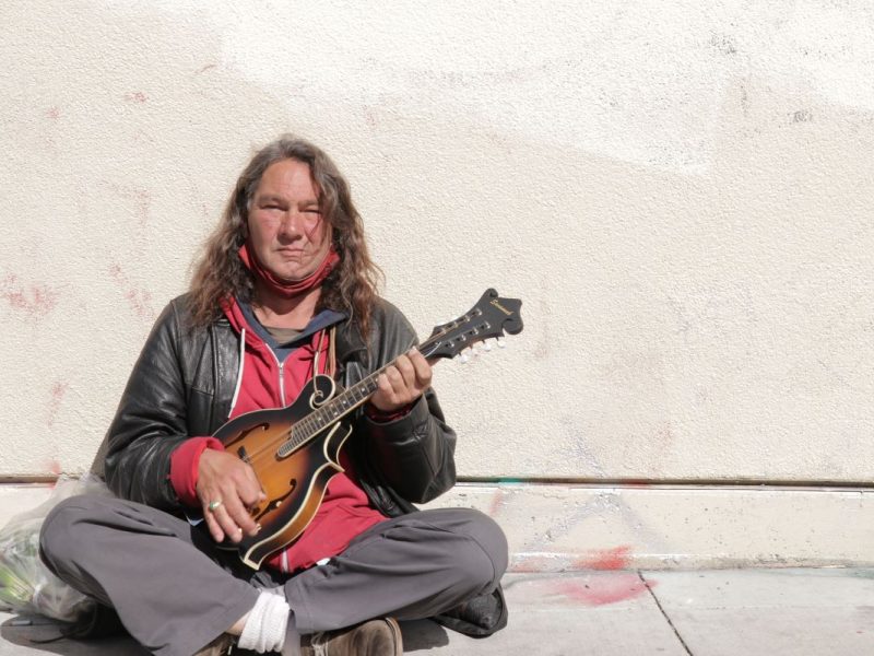 Max Johnson sits on the sidewalk on Bartlett Street playing his mandolin