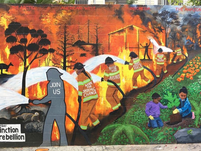 The new mural on clarion alley shows a line of firefighters holding a fire at bay from children playing in a lush forest landscape.