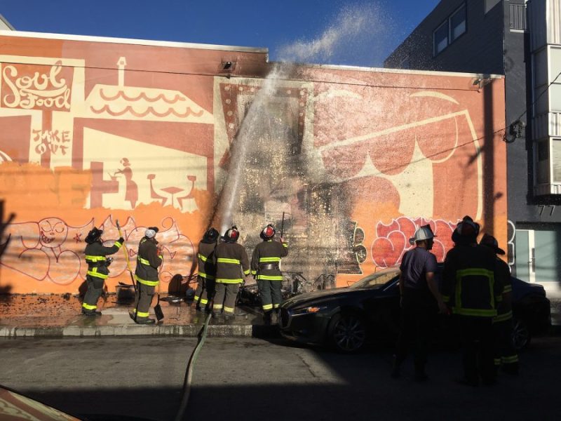 firefighters extinguish a fire started from grocery carts used as a barbecue against building wall