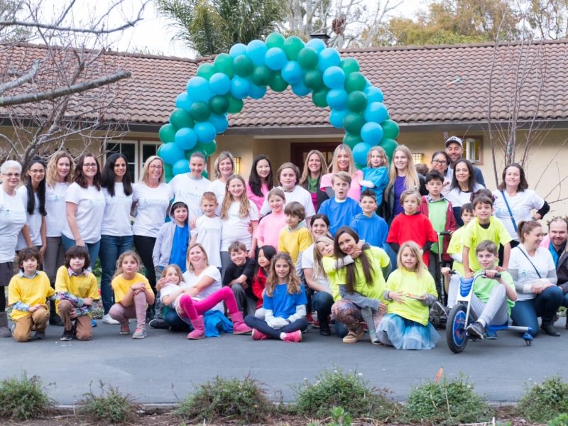 group of adults and children of all ages standing in front of a blue and green balloon archway for a rare disease event