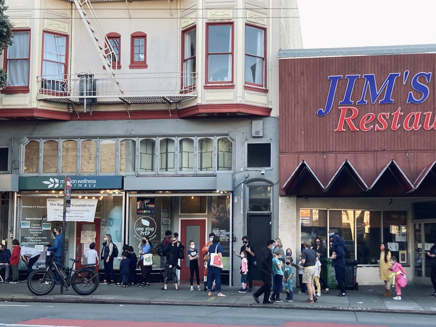 long line of children and their guardians on sidewalk outside mission wellness pharmacy