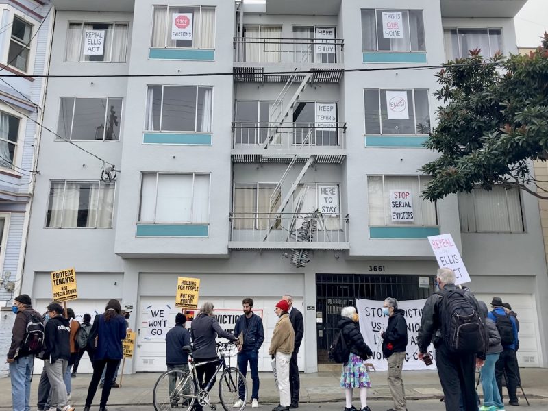 a group of people with signs picket an apartment building
