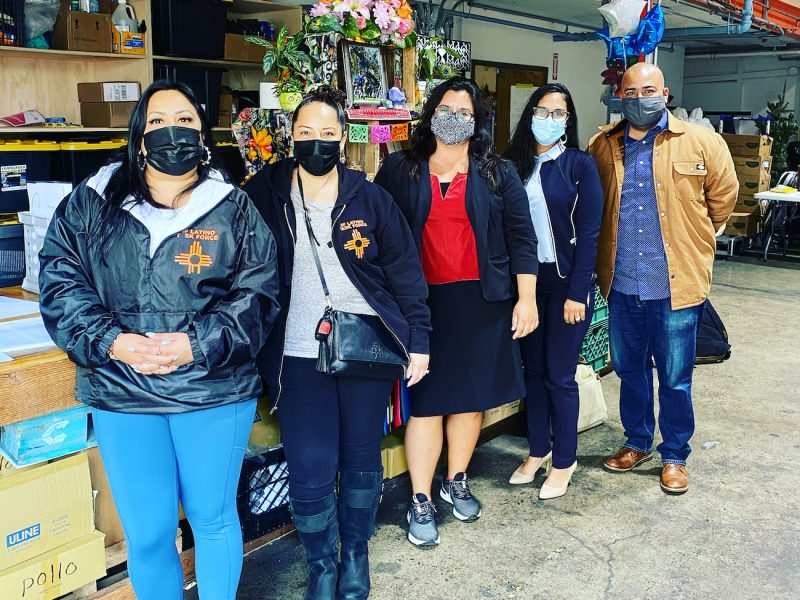 five people in masks stand in front of boxes and shelves with essential resource hub supplies
