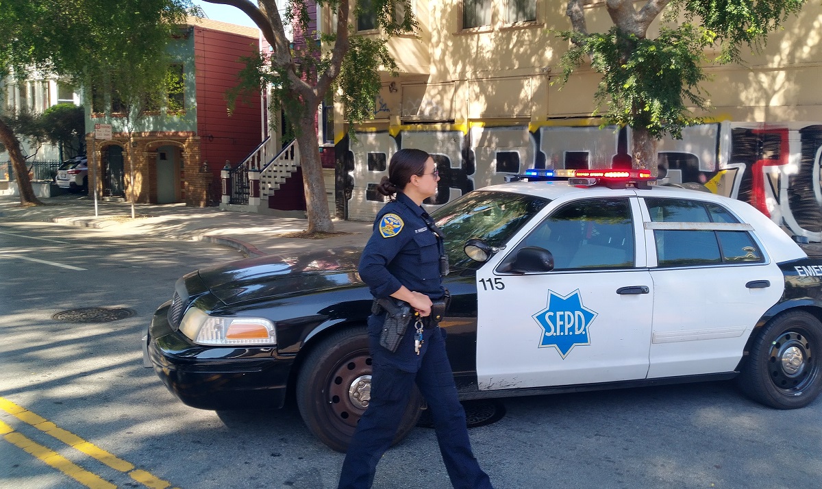 SFPD police officer walks past squad car.