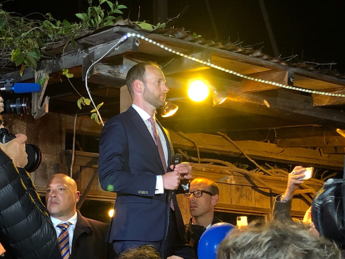 Chesa Boudin standing above a crowd with a microphone in his hand.