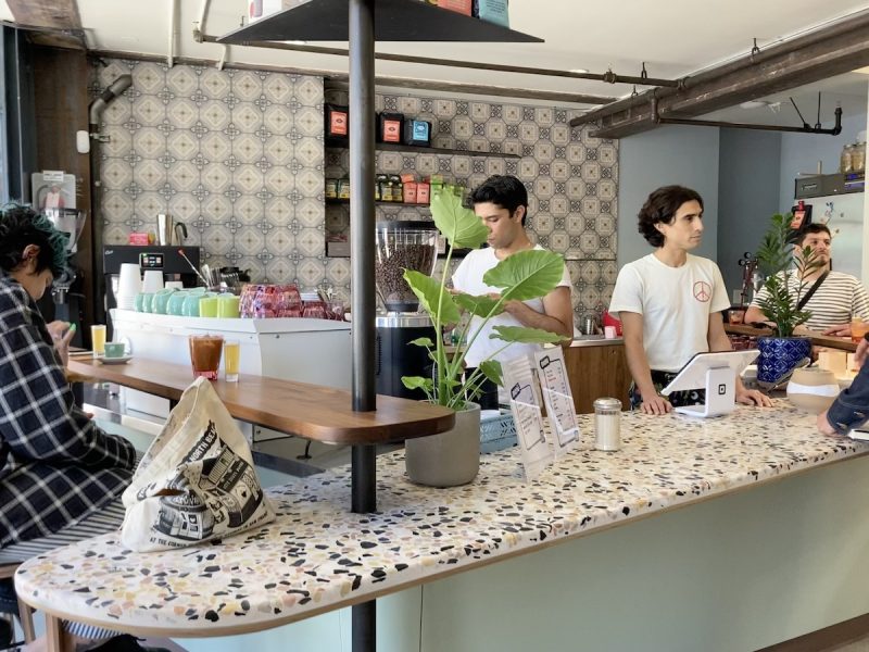 Two people in white work behind the counter of a cafe