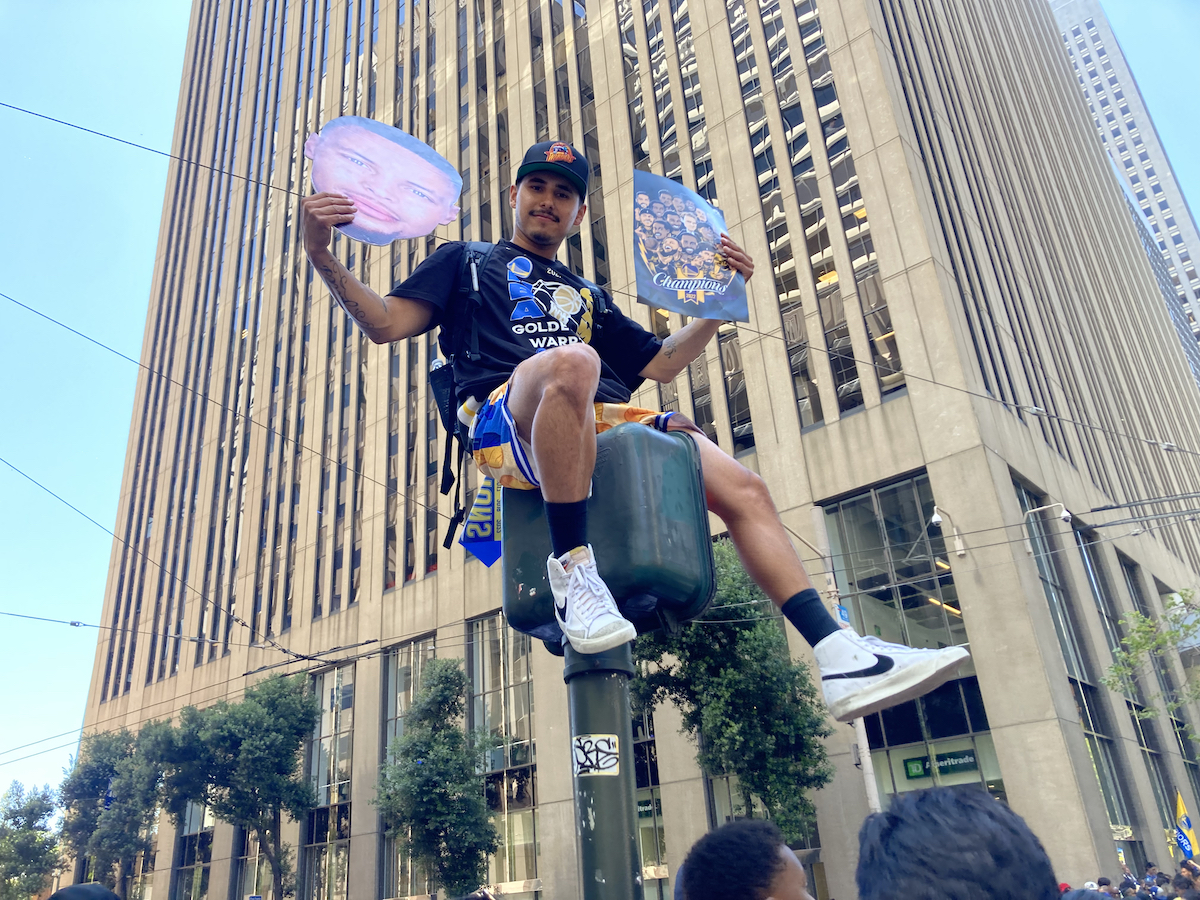 A man sits atop a pedestrian traffic signal
