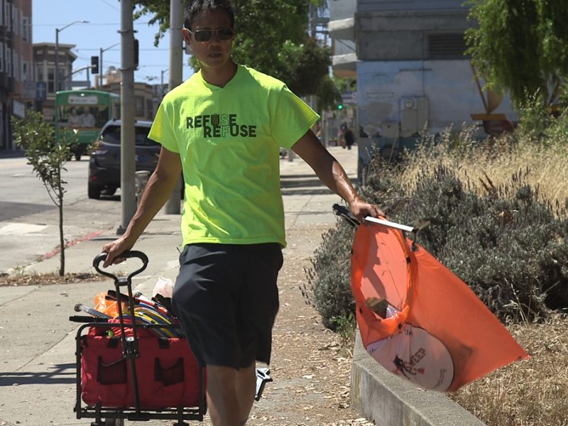 Vincent Yuen picks up trash while pulling his red cart.
