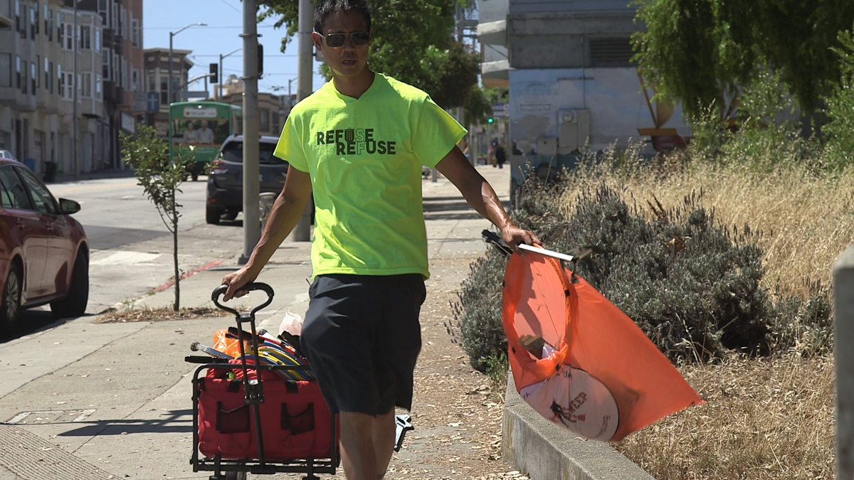 Vincent Yuen picks up trash while pulling his red cart.