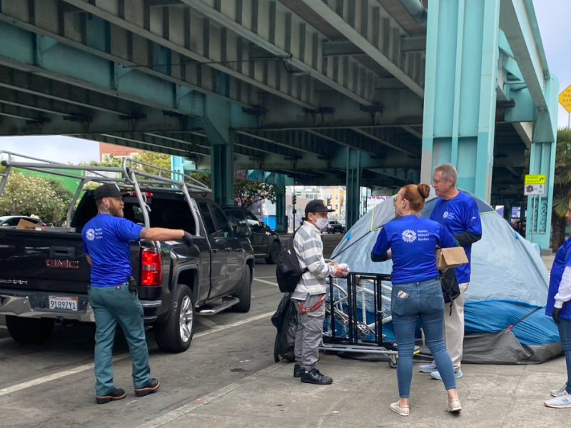 A group of volunteers for Healers Without Borders pass out socks to a homeless man at his tent.