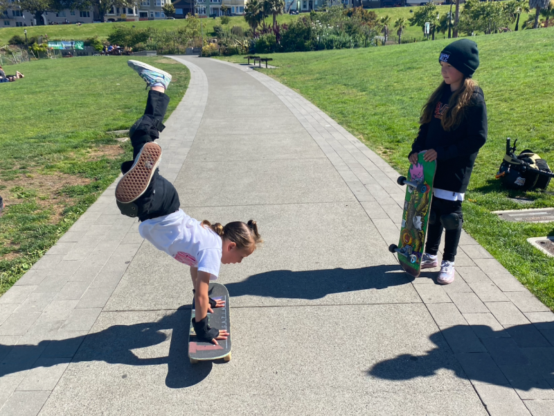 A 7-year old girl does a hand-stand on a skateboard