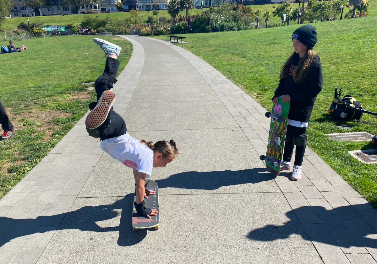A 7-year old girl does a hand-stand on a skateboard