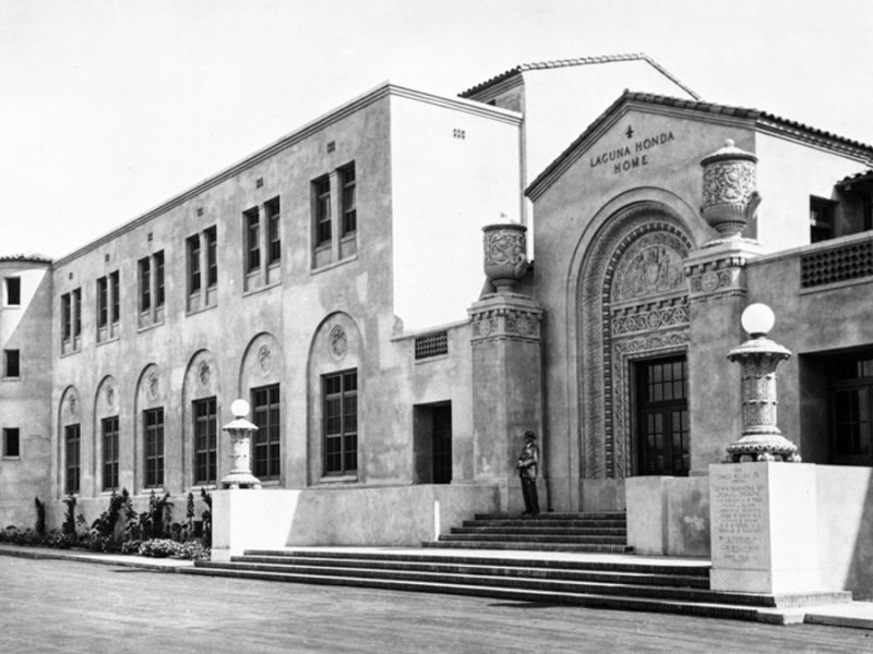 A stone-built building stands backlit against the sun. Words across the top read, Laguna Honda Hospital