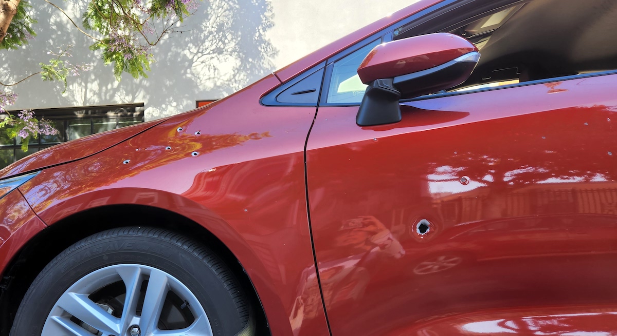 The front left of a red car with bullet holes in it