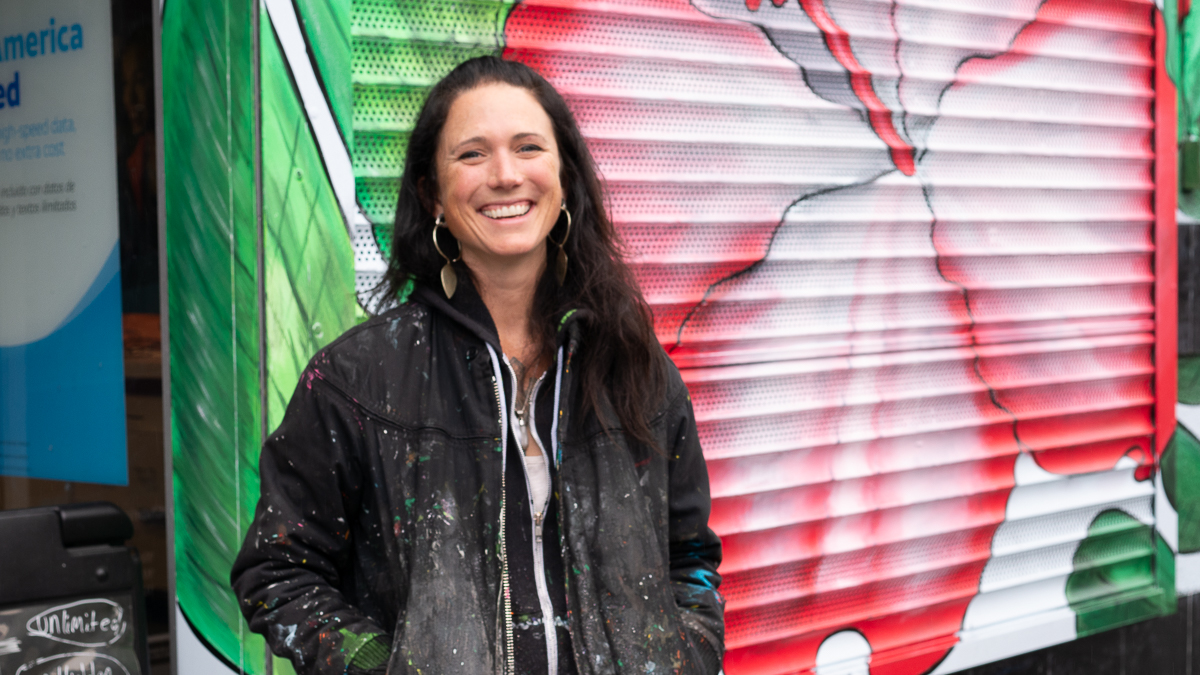 Amanda Lynn smiles in front of a pink Hibiscus flower painted on the garage door of the AT&T building