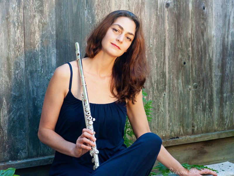 Rebecca Kleinmann with her flute, sitting against a wooden fence.
