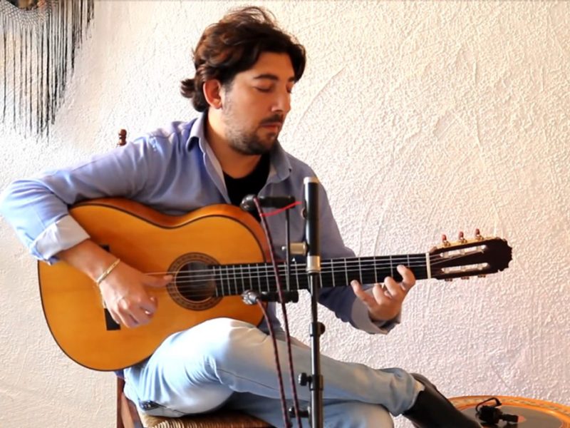 a man playing a guitar and siting on a stool.
