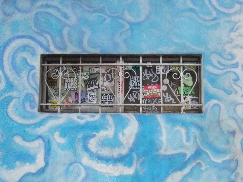 Photo of a window with graffiti surrounded by a wall that appears to look like the sky and clouds