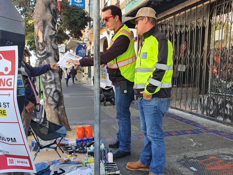 Public Works staffers hand a woman a flyer about how to obtain a permit to sell merchandise
