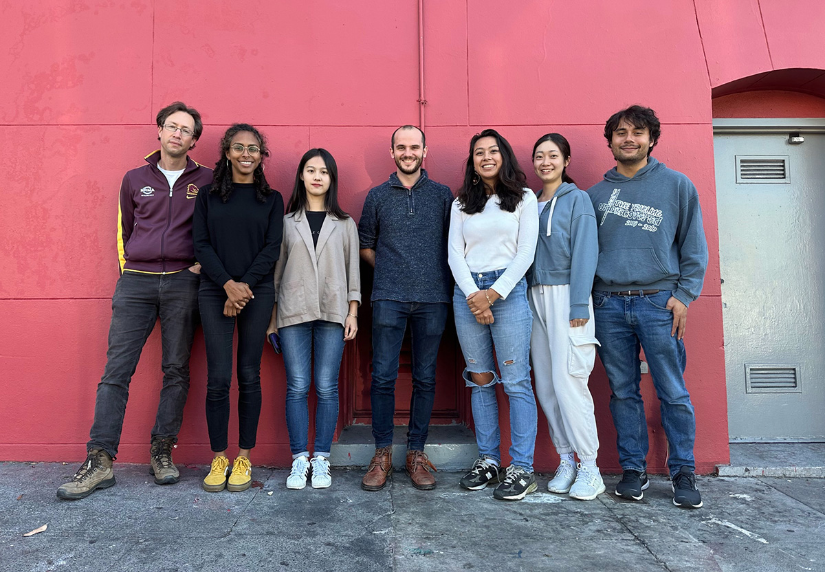 Seven people up against a pink-like wall.