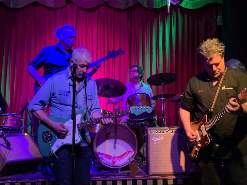 A band with four players, three on guitar and one on the drums
