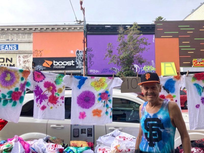 A man in front of air-brushed T-shirts.