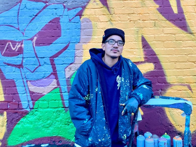 A young man with glasses standing in front of a mural