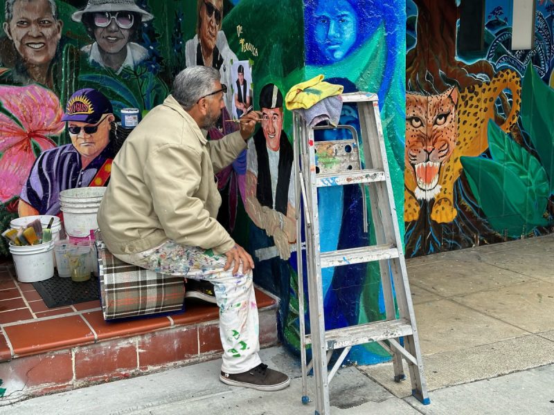 A man painting a mural. and a ladder nearby.