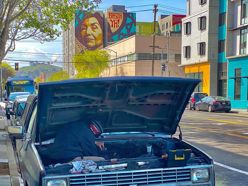 A car with its hood open and a mural in the background.