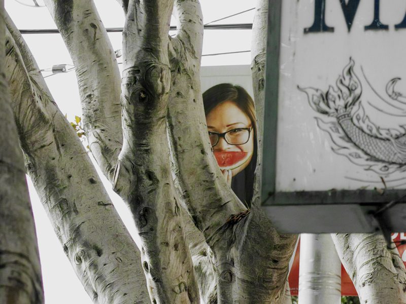 A woman with glasses and a watermelon in front of her mouth.