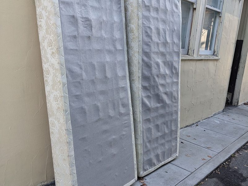 Two box springs up against an outside wall.