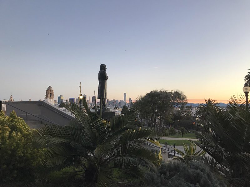 A statue of a man in a park, looking at the sunrise.
