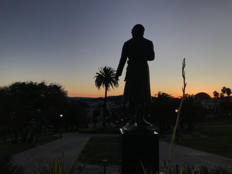 A statue of Hidalgo, his back to us, looking at the sunrise.