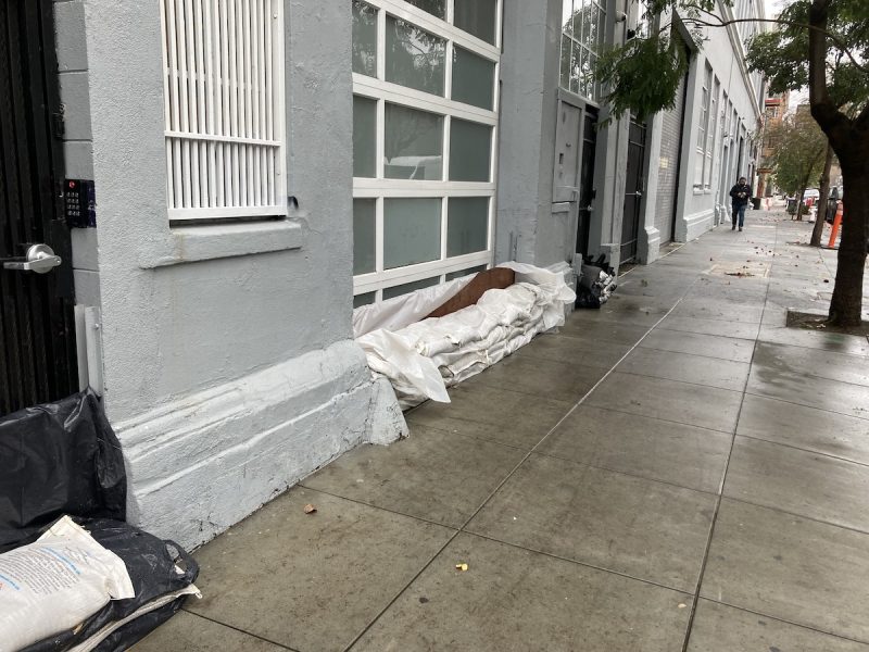 Sandbags and sheets of plastic block doors and garages. The street is wet.