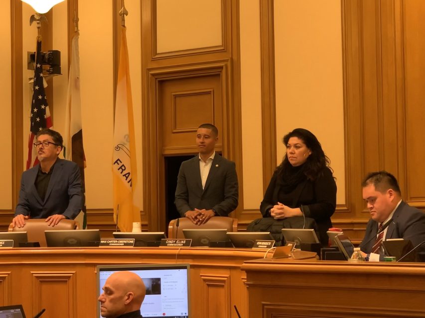 Three commissioners stand, another sitting.