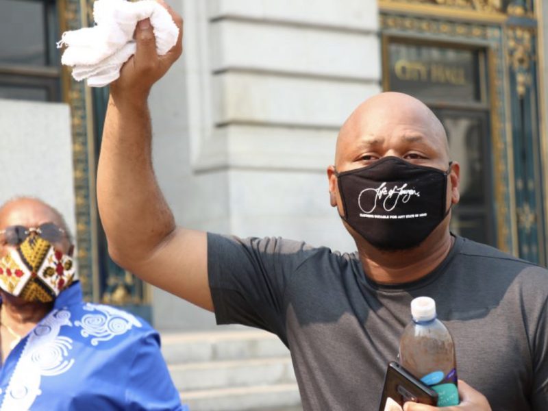 An African American person wearing a black face mask raises a white towel in the air