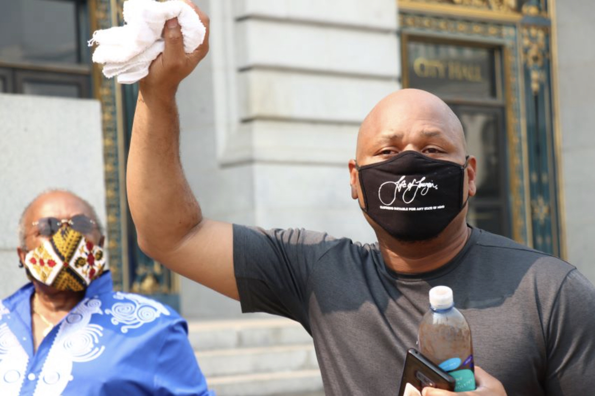 An African American person wearing a black face mask raises a white towel in the air