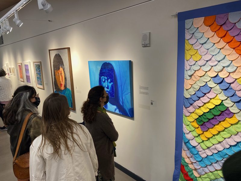 visitors in a gallery with paintings on the wall.
