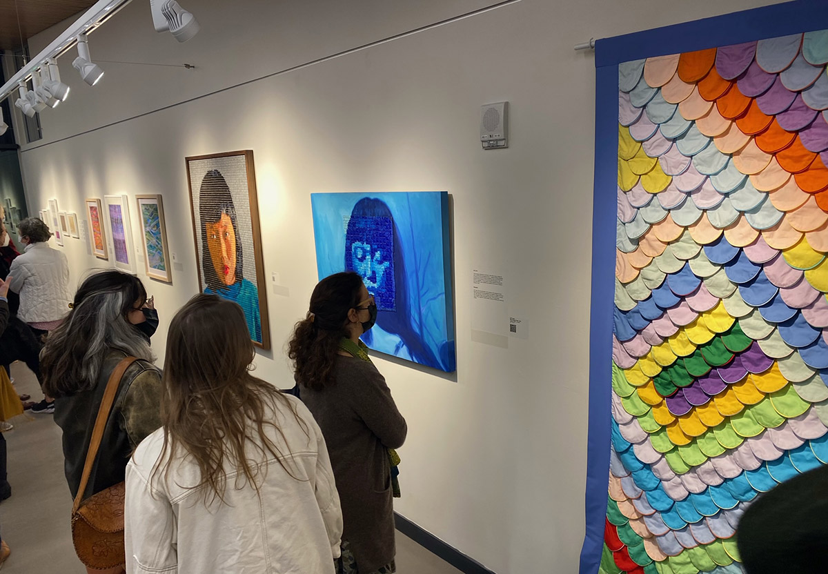 visitors in a gallery with paintings on the wall.