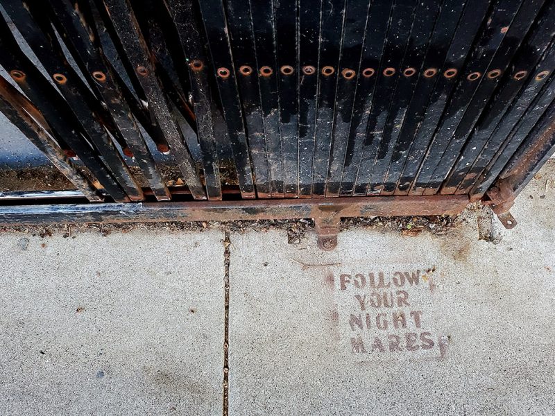 Graffiti stenciled on the sidewalk that reads Follow Your Nightmares.