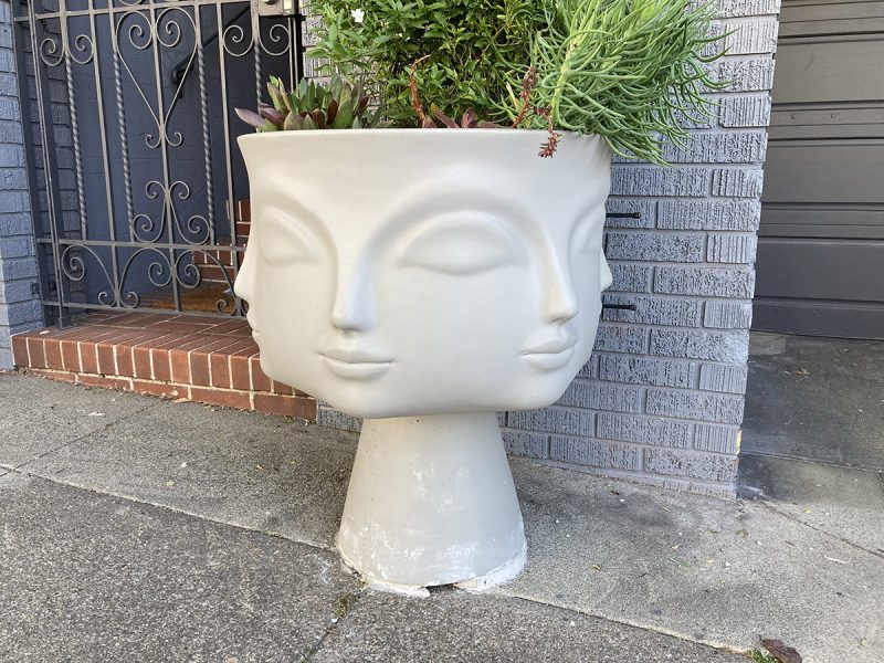 A white clay pot with profiles of women and a plant.